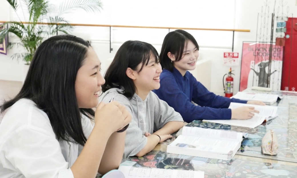 AIE国際高等学校神戸キャンパスの明るい教室で、笑顔でテキストを広げて学習に励む女子高校生たち。